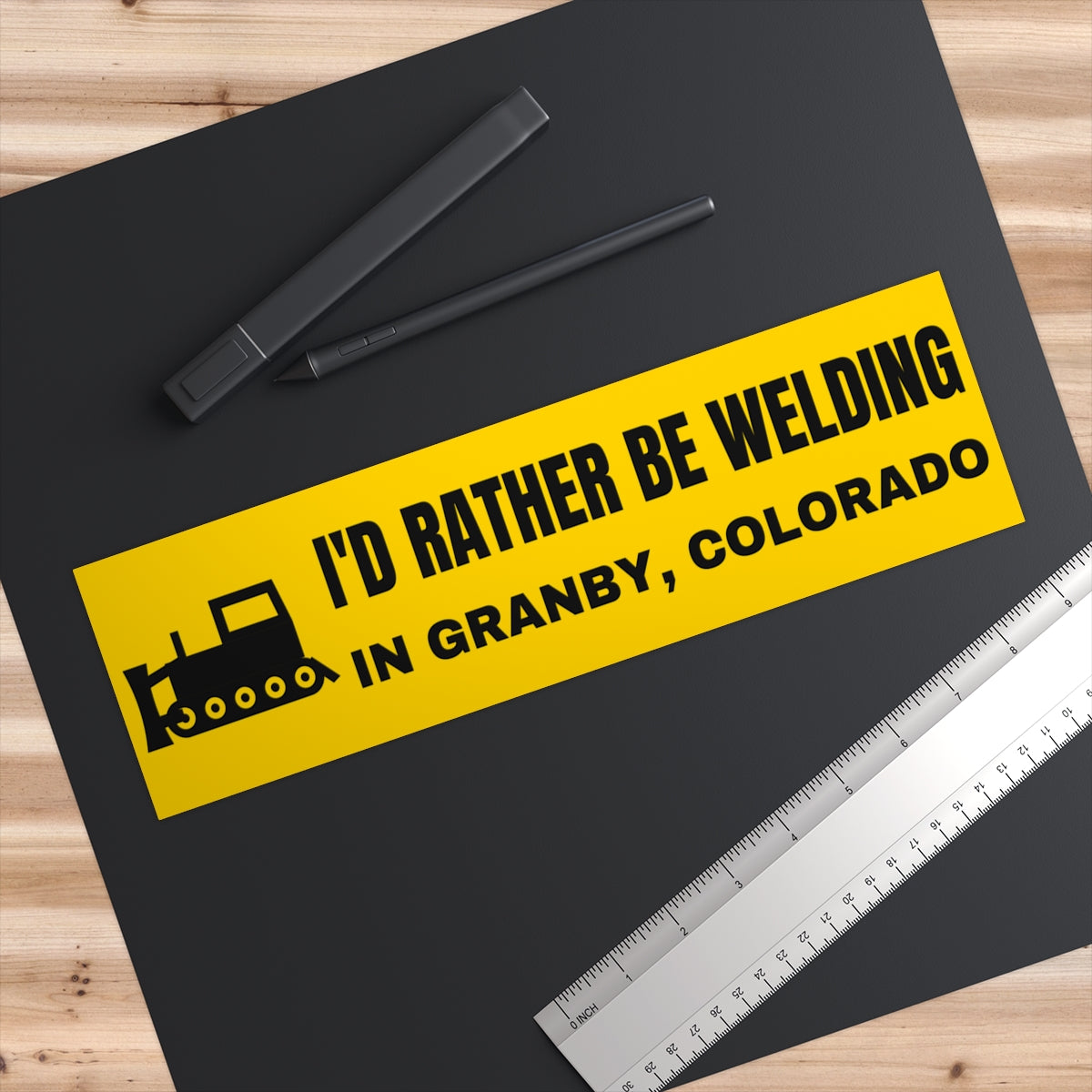 I'd Rather Be Welding in Granby, Colorado Bumper Sticker - on a desk next to a ruler, shown at true 11" x 3" scale